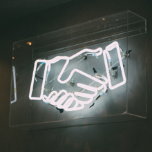 Eine im dunkeln leuchtende Installation zeigt zwei in einander verschränkte Hände.