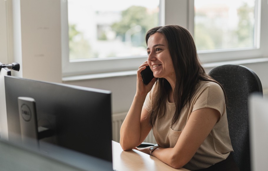 Eine 25-jähringe Mitarbeiterin, Consultant und Scrum Master in Cluj, sitzt am Schreibtisch und telefoniert und teilt ihre Erfahrungen in der agilen Entwicklung von Websites mit TYPO3.