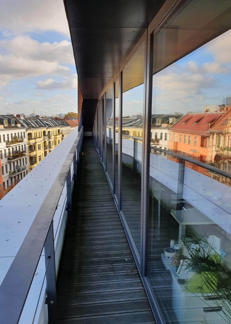 Die Fensterfront mit Panoramablick in unserem Büro am Standort Berlin. Im Glas spiegeln sich die Dächer der Stadt wider.